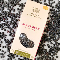 Women's Bean Project black bean soup mix laid on a table with black bean scattered around the box
