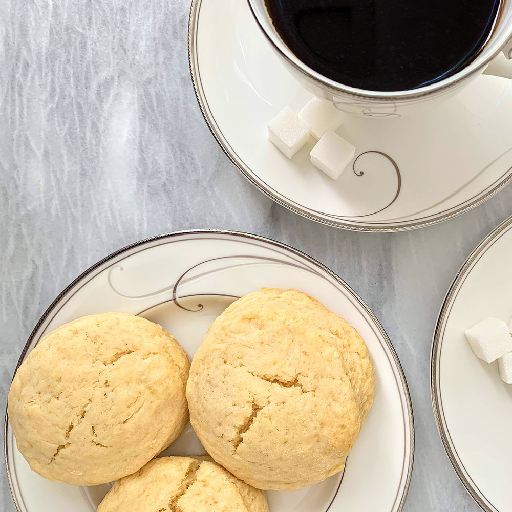Women's Bean Project cream scones on a plate with a cup of black coffee on the side