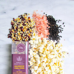 Women's Bean Project Rainbow popcorn laid out on a table with pre-popped popcorn and Himalayan pink salt and pepper kernels.