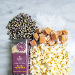 Women's Bean Project blue popcorn and salted caramel seasoning laid out next to pre-popped popcorn and wedges of salted caramel.