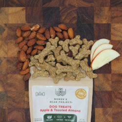 Women's Bean Project Apple and Toasted Almond dog treats wedged between almonds and apple slices on a brown table.