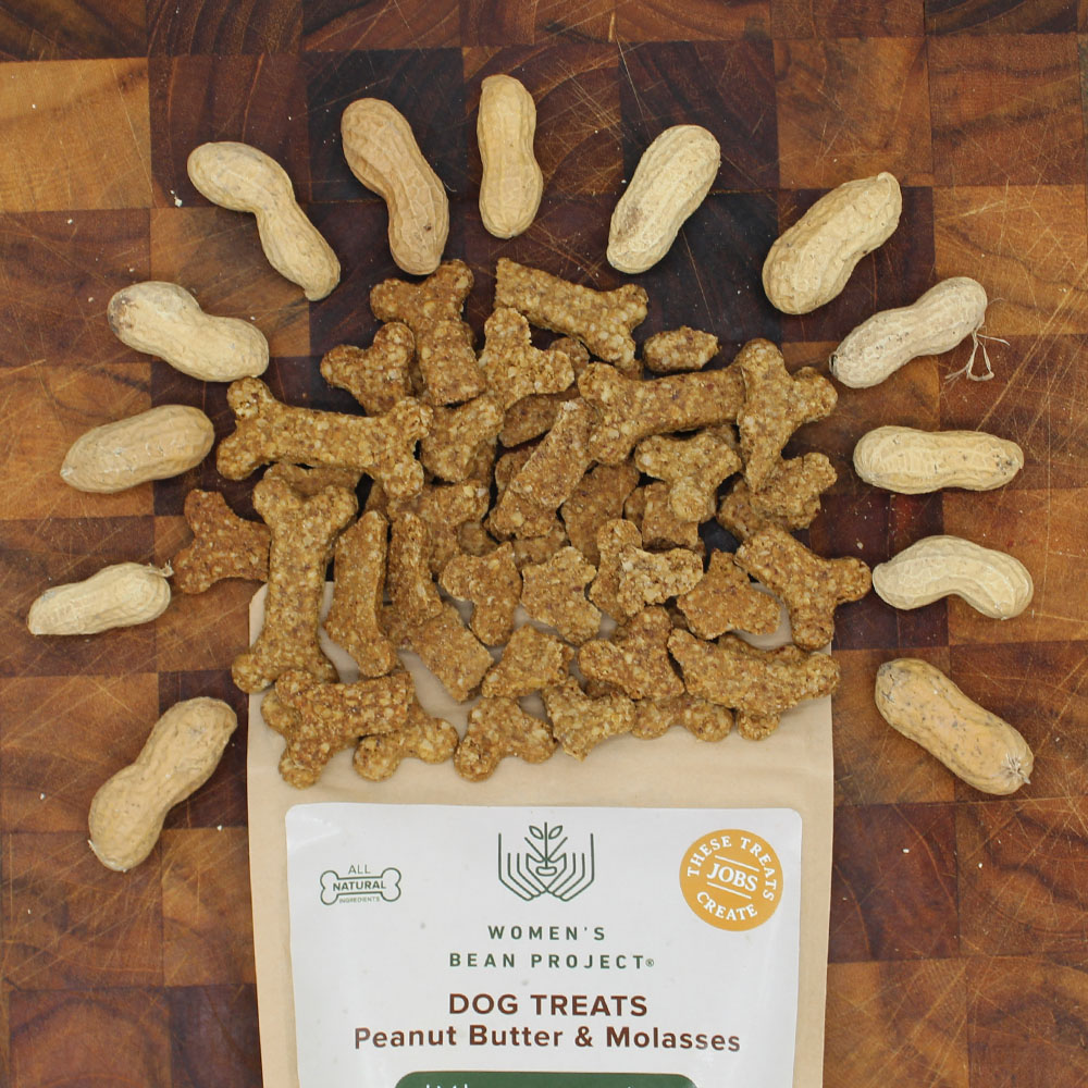 Women's Bean Project Peanut Butter and Molasses dog treats laid on a brown table between whole peanuts