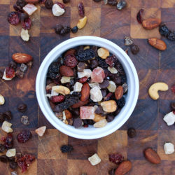 Women's Bean Project Ginger Zing trail mix in a white bowl on a table scattered with trail mix.