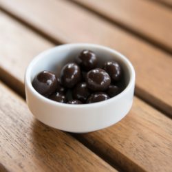 Women's Bean Project chocolate covered espresso beans in a white dish on a brown table.