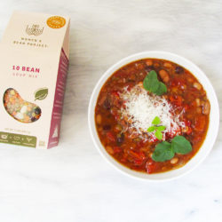 Women's Bean Project 10 Bean Soup prepared alongside itself in the packaging on a white table.