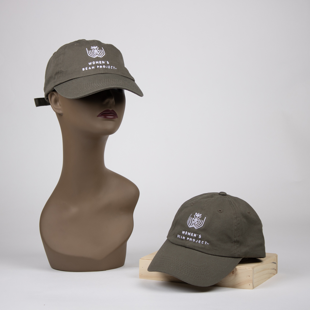A sage green ballcap with the Women's Bean Project logo embroidered on the front in white.