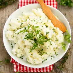 A bowl of vegan garlic mashed potatoes on a red towel and wooden table.