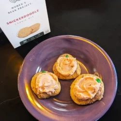 Frosted pumpkin snickerdoodles on a place next to a box of Women's Bean Project Snickerdoodle Cookie Mix.